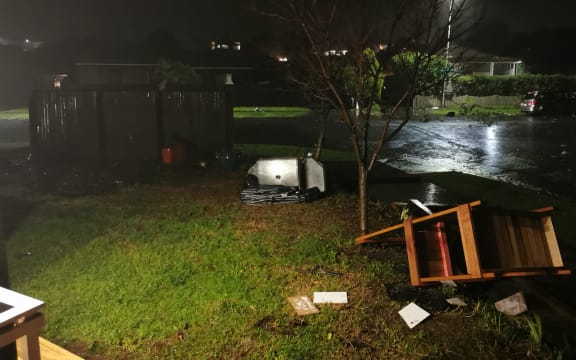 Debris strewn across the ground, including a barbeque and lawn chairs.