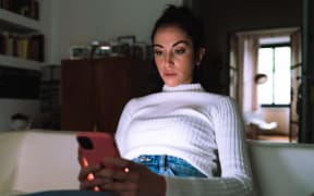 Young woman looking at her phone at home (Photo by Eugenio Marongiu / Cultura Creative / Connect Images via AFP)