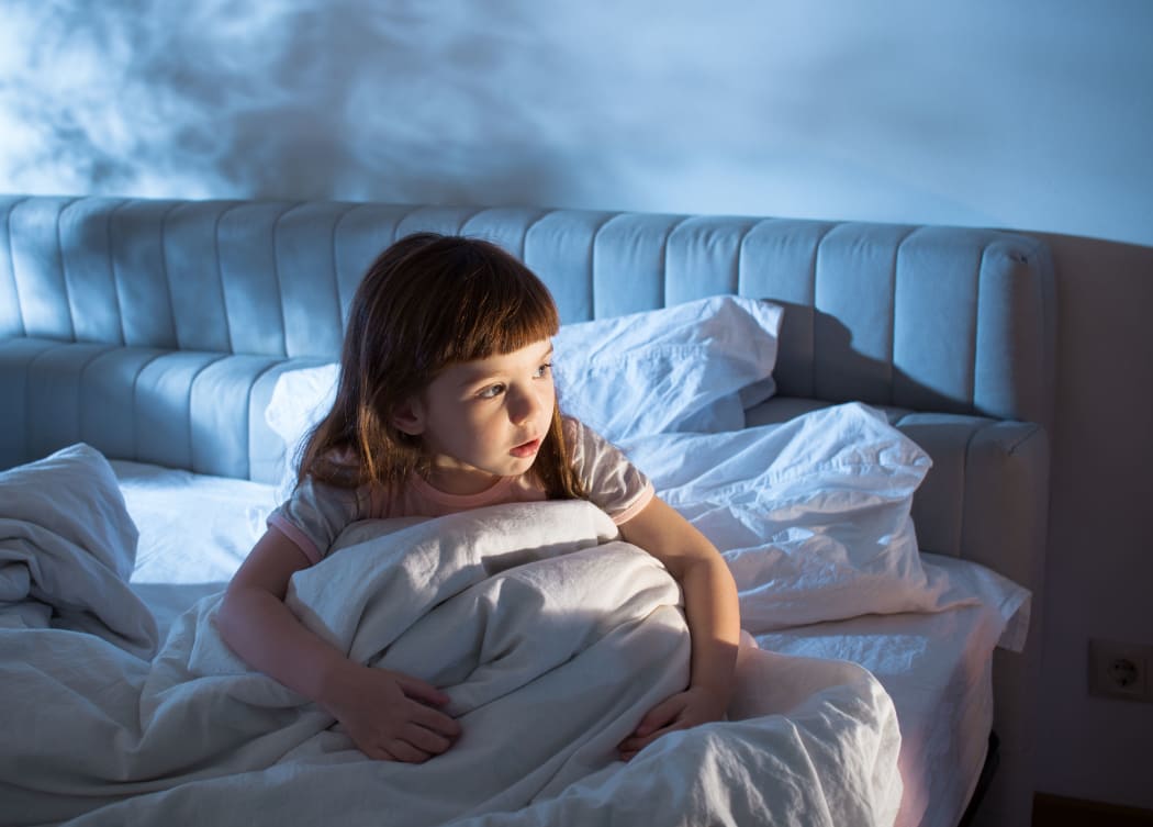 A photo of a girl of 4 years at night time who looks afraid to go to sleep