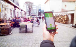 Vaccinated person using a digital vaccination or immunisation certificate on a smartphone at a restaurant terrace.