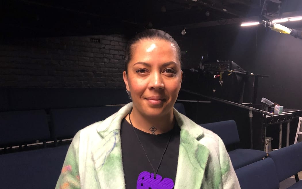 Portrait of Cat Ruka. Ruka is standing in a theatre space, looking directly at the camera.