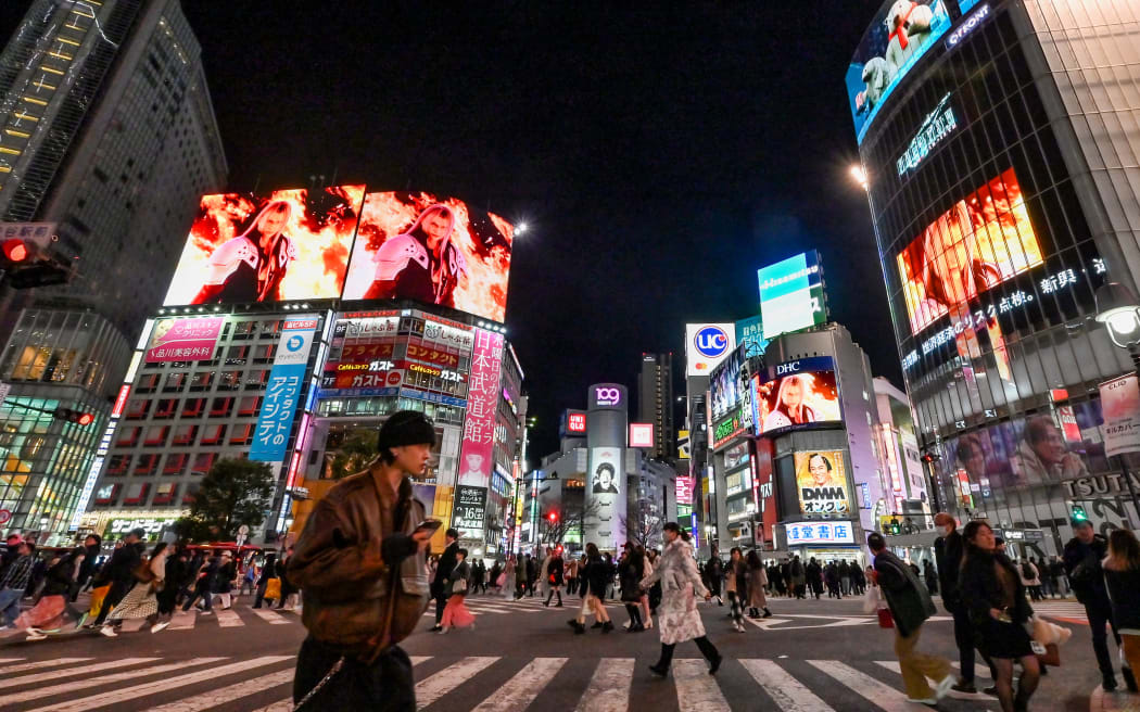 Pedestrians walk through Shibuya Crossing as a promotional video (above) showing imagery from "Final Fantasy VII Rebirth" - the latest release of the video game franchise developed and published by Japanese company Square Enix - is displayed on different screens in the Shibuya area of Tokyo on February 27, 2024. Final Fantasy VII Rebirth is set to be released on February 29.