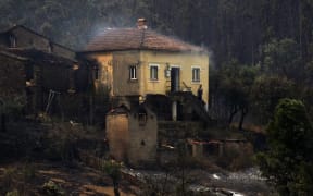 A  man stands in the stairway of a house with smoke billowing from the roof in an area devastated by a wildfire in Canical, near Alvares.