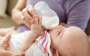 family, parenthood and people concept - close up of father feeding little daughter with baby formula from bottle at home