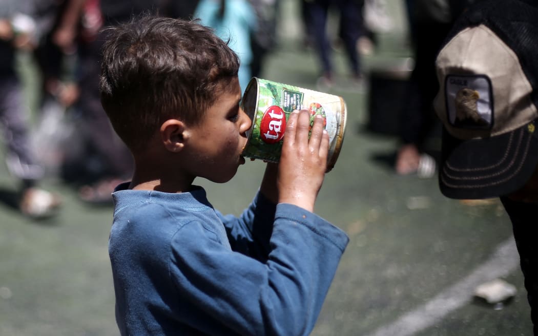 A Palestinian child eats his portion of a hot meal at a free food distribution point at the Nuseirat refugee camp in the central Gaza Strip on April 19, 2025. (Photo by Eyad BABA / AFP)