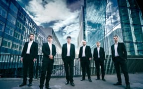 Gesualdo Six in black suits against a blue & white cityscape