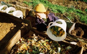 A woman deposits her food waste on to a composting pile.