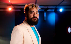 Noah Slee standing in the foreground wearing a white sports coat and azure shirt