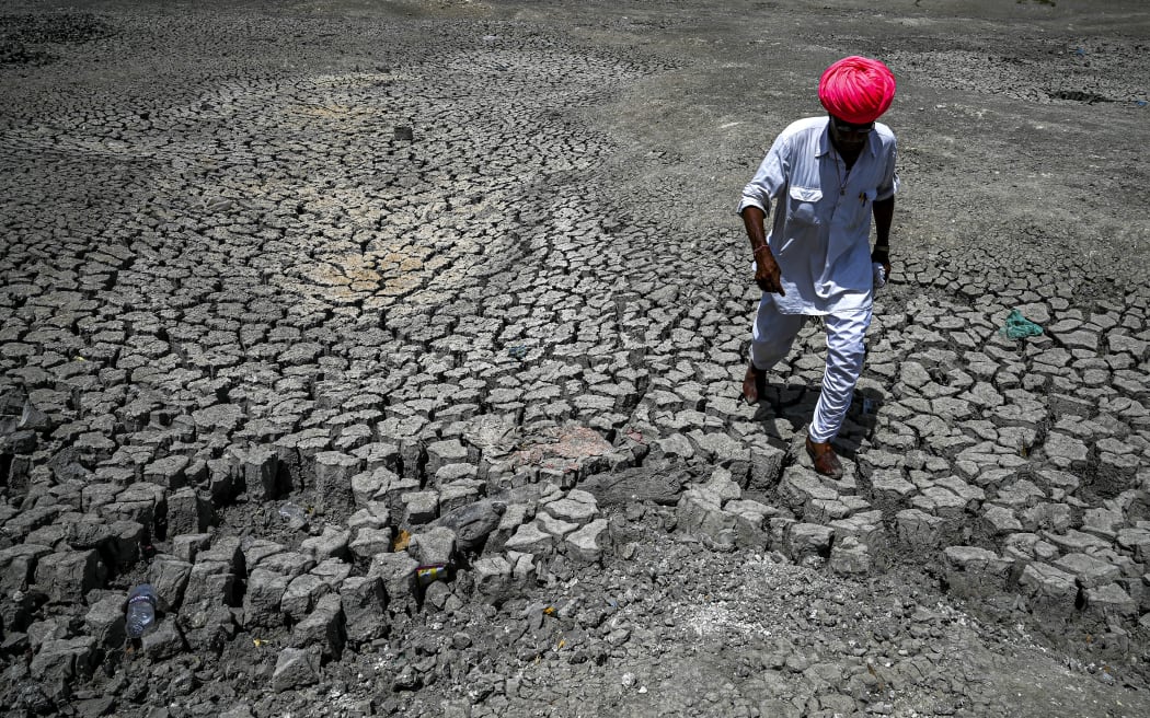 A villager walking through the cracked bottom of a dried-out pond on a hot summer day at Bandai village in Pali district in India's desert state of Rajasthan. Every day dozens of villagers, mostly women and children, wait with blue plastic jerry cans and metal pots for a special train bringing precious water to people suffering a heatwave in India's desert state of Rajasthan.