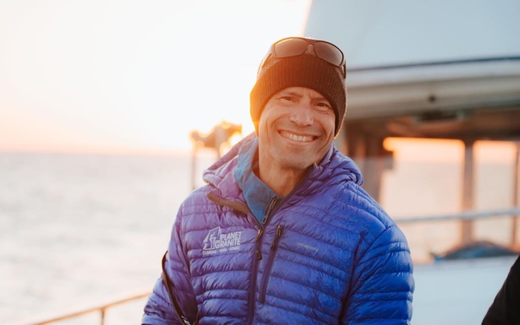 Man in his 40s sitting on the bow of a boat holding a long-lensed camera.