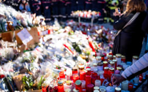 People gather around a makeshift memorial to pay their respects by laying flowers, candles and messages near the Constellation bar, on January 4, 2026, in Crans-Montana in honour of the victims of the fire that ripped through the venue in the luxury Alpine ski resort on New Year's Eve. Authorities investigating the New Year's blaze in the Swiss resort of Crans-Montana have identified 24 of the 40 people killed, including 11 minors and six foreign nationals, police said on January 4, 2026. Also 119 were injured during the fire, most of them seriously, according to the latest toll. (Photo by MAXIME SCHMID / AFP)