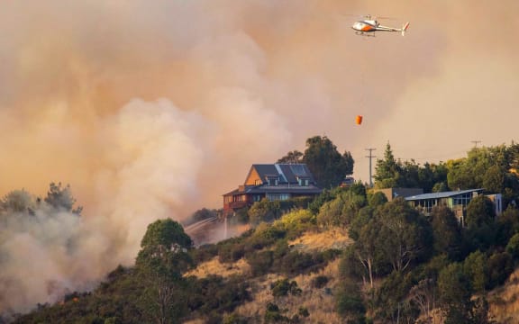 Firefighters try to save a house from fire on Port Hills in Christchurch. The fires destroyed nine houses and one helicopter pilot died fighting the blaze.
