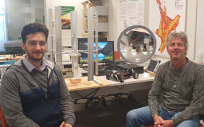 Soheil Mohseni and Alan Brent work with sustainable energy systems. There are mini versions of a vertical wind turbine and a solar concentrator on the desk behind them.