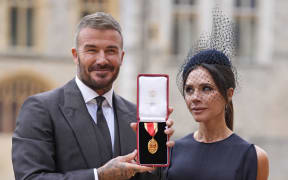 Former England footballer David Beckham (L) poses next to his wife, singer and fashion designer Victoria Beckham (R), with his medal after being appointed as a Knight Bachelor (Knighthood) for services to sport and charity at an investiture ceremony at Windsor Castle on 4 November, 2025.