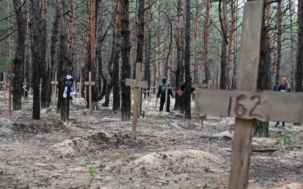 Ukrainian police officers walk among crosses in a forest on the outskirts of Izyum, eastern Ukraine on 16 September, 2022. Ukraine said it had counted 450 graves at just one burial site near Izyum after recapturing the eastern city from Russian forces.