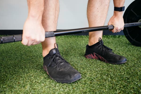 A man lifts a barbell while wearing flat black sneakers.