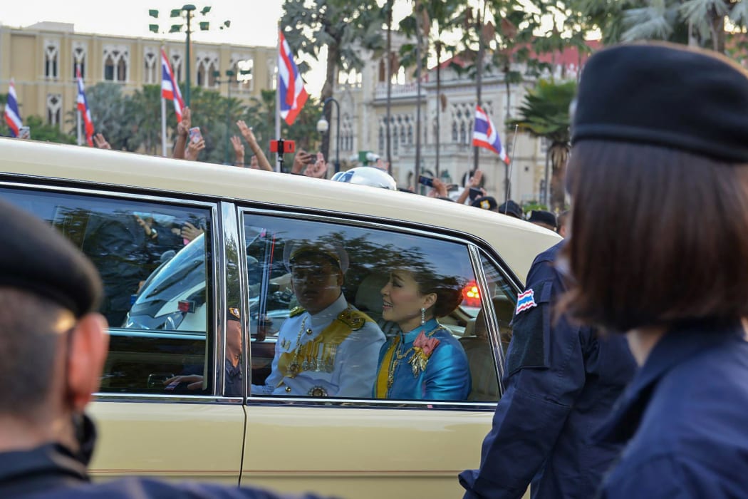 Thailand's Queen Suthida and Prince Dipangkorn Rasmijoti  are driven in a motorcade past a pro-democracy rally, as anti-government protesters (back) hold up their three-finger salute, in Bangkok on October 14, 2020.
