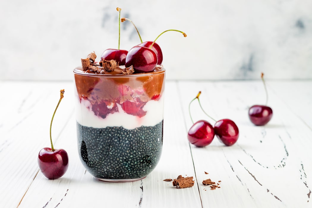 Healthy Black Forest dessert. Black activated charcoal chia pudding with cherries, coconut cream and chocolate. Vegan creamy breakfast.