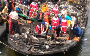 Rescuers search the charred passenger boat which caught fire off the coast of Jakarta, killing 23 people.