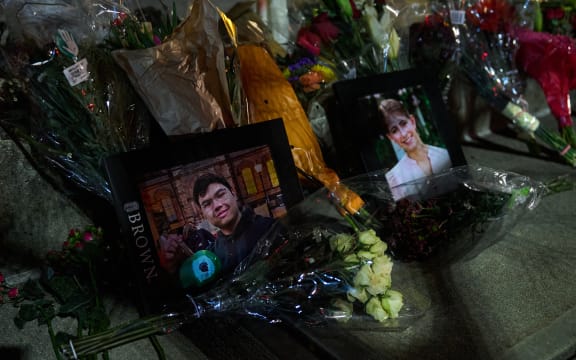 Framed photos of mass shooting victims Mukhammad Aziz Amurzokov and Ella Cook are seen at a makeshift memorial near Brown University in Providence, Rhode Island, on December 15, 2025. A gunman remained at large after a weekend mass shooting at elite Brown University left two dead and nine wounded, with US authorities releasing new footage of a masked "person of interest" captured on surveillance cameras. The shooting took place December 13 in a building where exams were underway on the Ivy League campus in Providence, Rhode Island when a man with a rifle burst in and opened fire before fleeing. (Photo by Bing Guan / AFP)