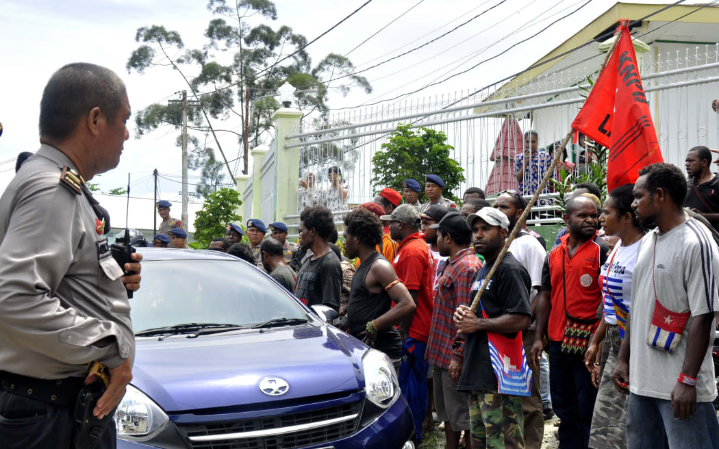 Indonesia police officer (L) stands guard as Papuan pro-independence activist Filep Karma's supporters hold a rally outside prison in Abepura, Papua province, on November 19, 2015 to welcome their leader's freedom