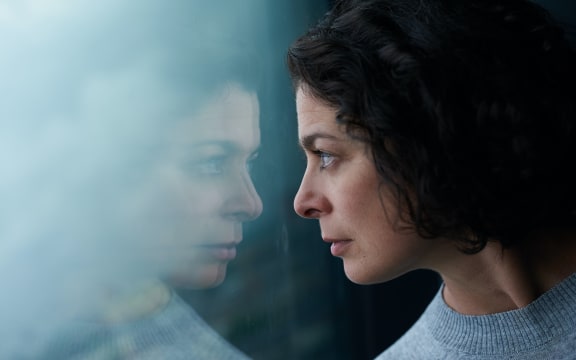 woman with black here looking out a window with reflection