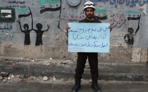 In the city of Aleppo, Syrian civil defense team members hold banners as they gather to protest for civilians who starved to death in Madaya.