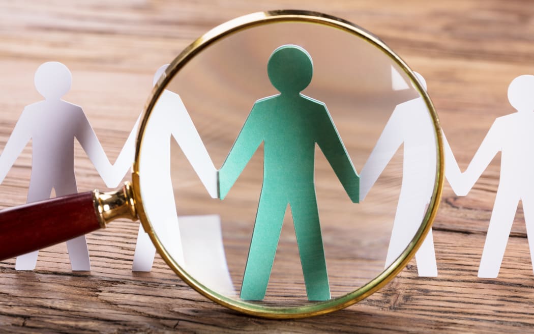 Magnifying Glass On Cut-out Figures On Wooden Desk