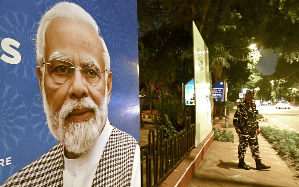 Indian security personnel stands guard next to G20 communication billboard with a portrait of India' prime minister Narendra Modi days ahead of its commencement in New Delhi on September 7, 2023.