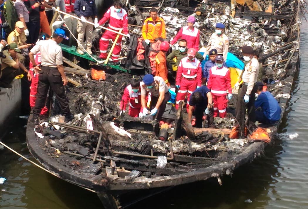 Rescuers search the charred passenger boat which caught fire off the coast of Jakarta, killing 23 people.