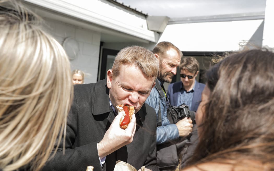Chris Hipkins enjoys a sausage after helping out on the barbecue at Ara Ake in New Plymouth while on the election campaign trail on 25 September 2023.