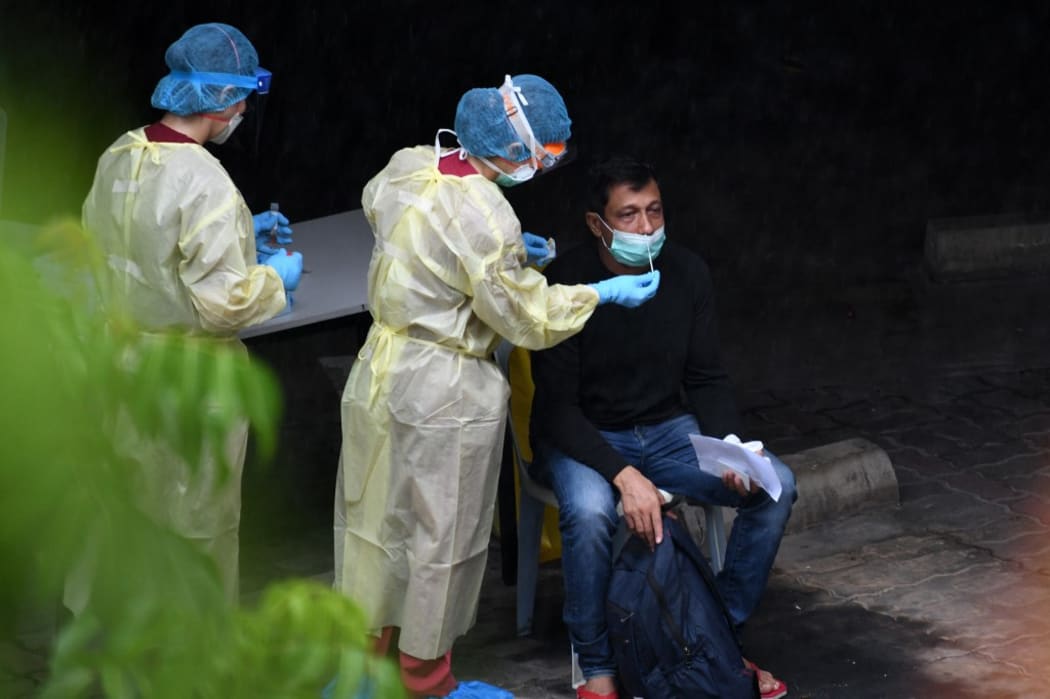 A healthcare worker dressed in personal protective equipment collects a nasal swab sample from a migrant worker for testing for the COVID-19 novel coronavirus at a foreign workers' domitory in Singapore on April 27, 2020.