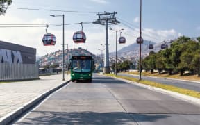 An image of a cable car crossing a road above a bus.