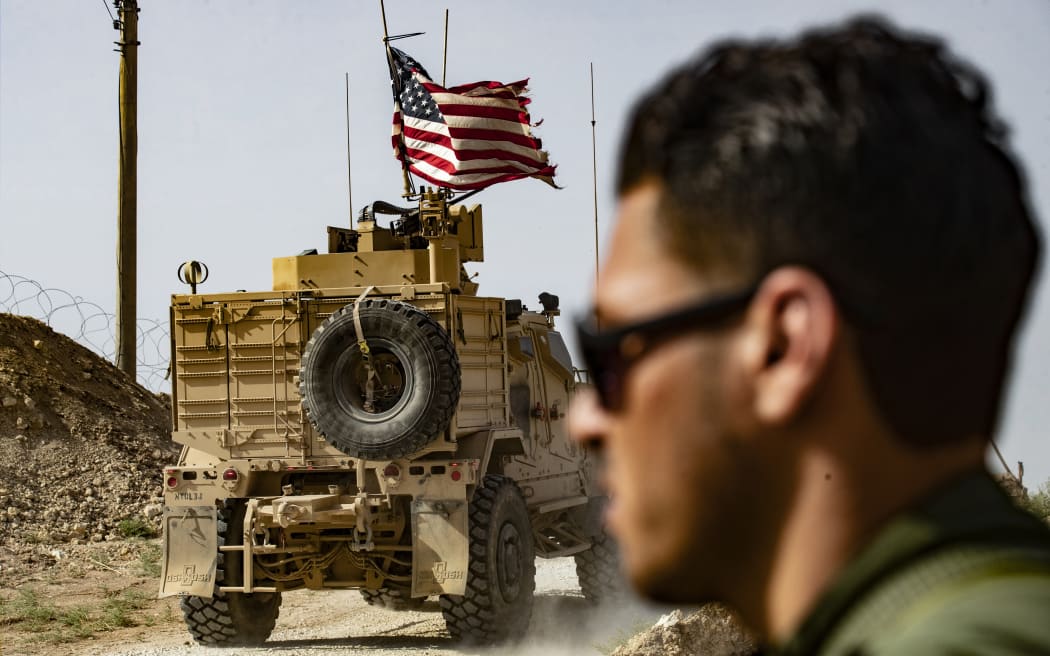 A US soldier sits atop an armoured vehicle during a demonstration by Syrian Kurds against Turkish threats next to a base for the US-led international coalition on the outskirts of Ras al-Ain town in Syria's Hasakeh province near the Turkish border on 6 October 2019.