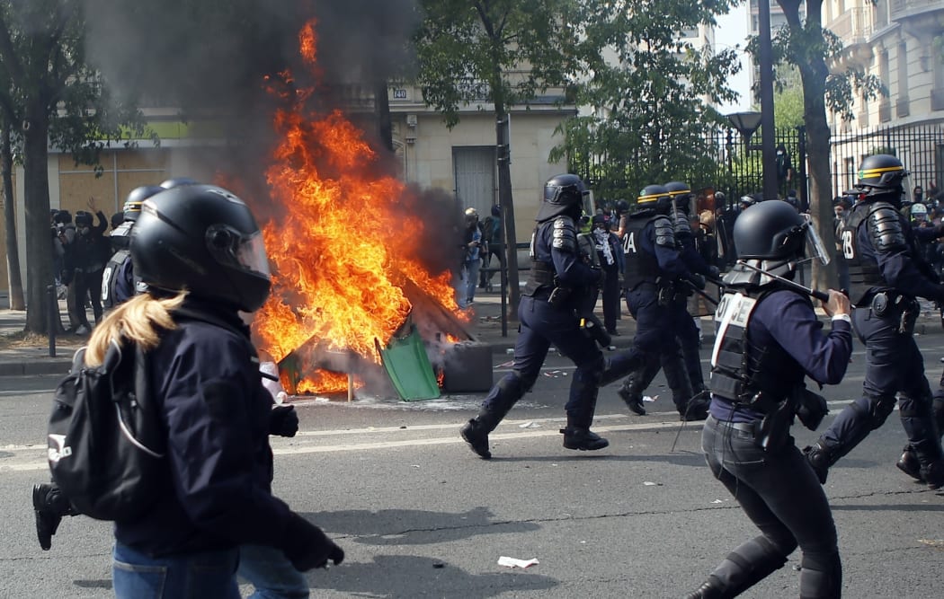 Police officers pass by burning garbage as they confront demonstrators during a May Day rally in Paris.