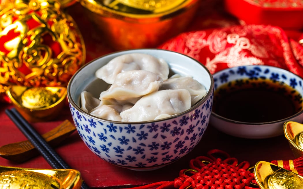 a bowl of chinese dumplings with ingot and red knot as background