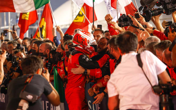 Charles Leclerc celebrates with Ferrari teammates and fans.