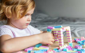 Little beautiful child playing with toy plastic building blocks, sitting at the table. Small girl busy with fun creative leisure activity. Development of fine motor skills for children.