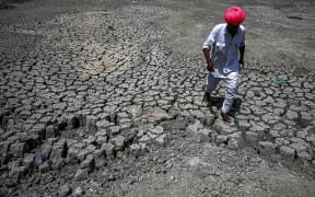 A villager walking through the cracked bottom of a dried-out pond on a hot summer day at Bandai village in Pali district in India's desert state of Rajasthan. Every day dozens of villagers, mostly women and children, wait with blue plastic jerry cans and metal pots for a special train bringing precious water to people suffering a heatwave in India's desert state of Rajasthan.