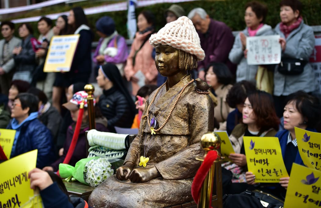 Protestors sit next to a statue (C) of a South Korean teenage girl in traditional costume called the "peace monument" for former "comfort women" who served as sex slaves for Japanese soldiers during World War II in Seoul on November 11, 2015.