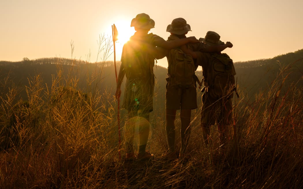 silhouette of male students standing and hugging each other in the grass on the mountain Boy Scouts rejoice at rock climbing success in the evening at sunset.
