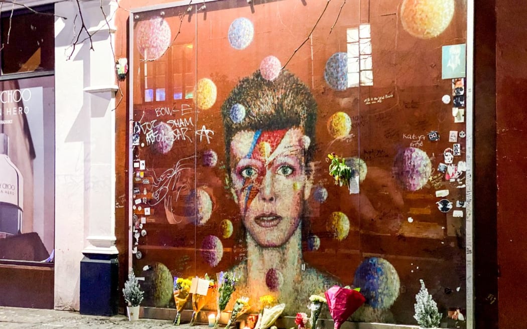 Flowers and candles are left past a mural depicting the cover of Aladdin Sane, to remember the firth anniversary of the death of the British iconic musician David Bowie, in Brixton, south London on January 10, 2021.