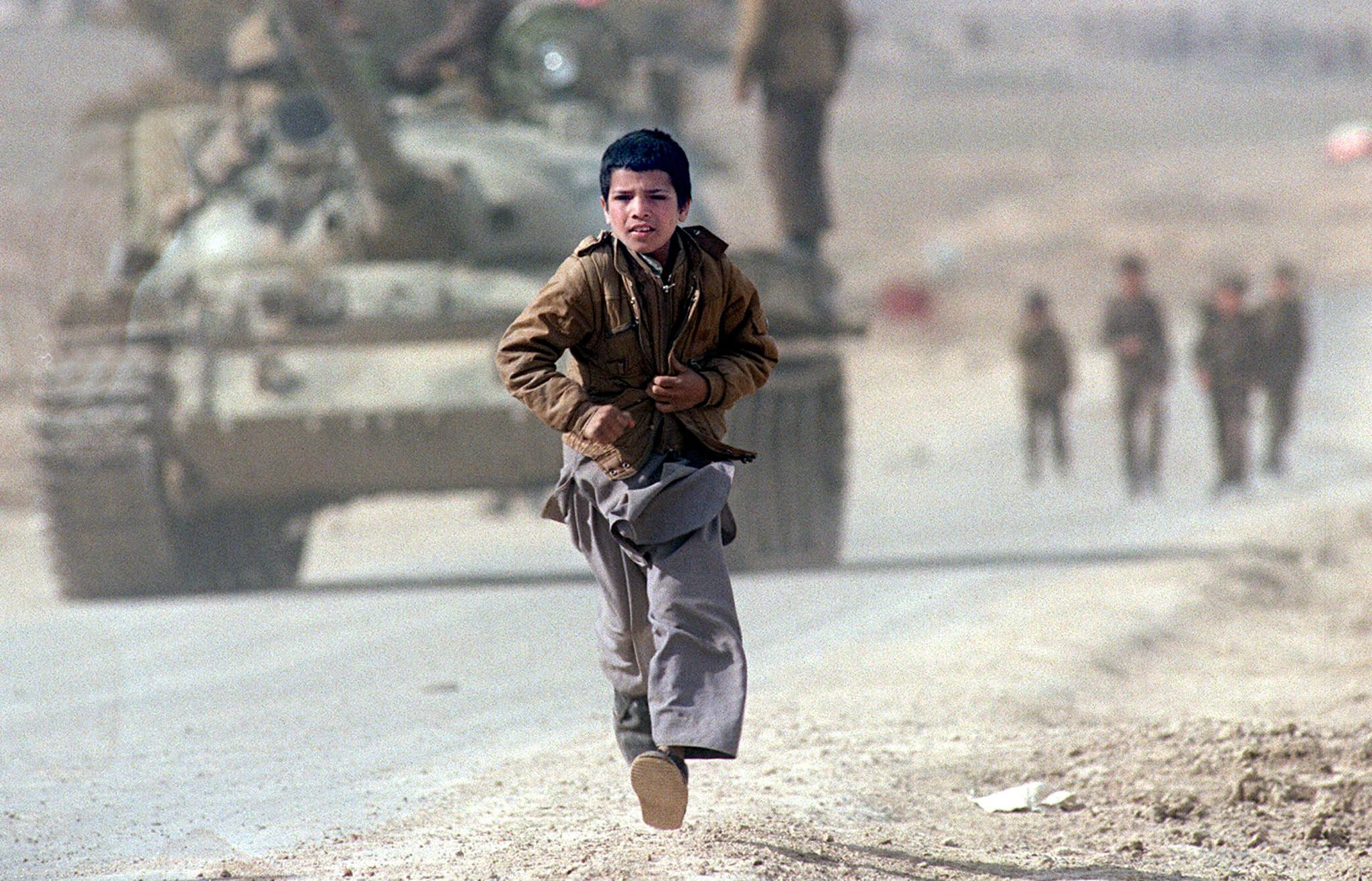 A boy runs after a bus in the Afghan capital Kabul in April 1989 as Soviet tanks patrol the streets.
