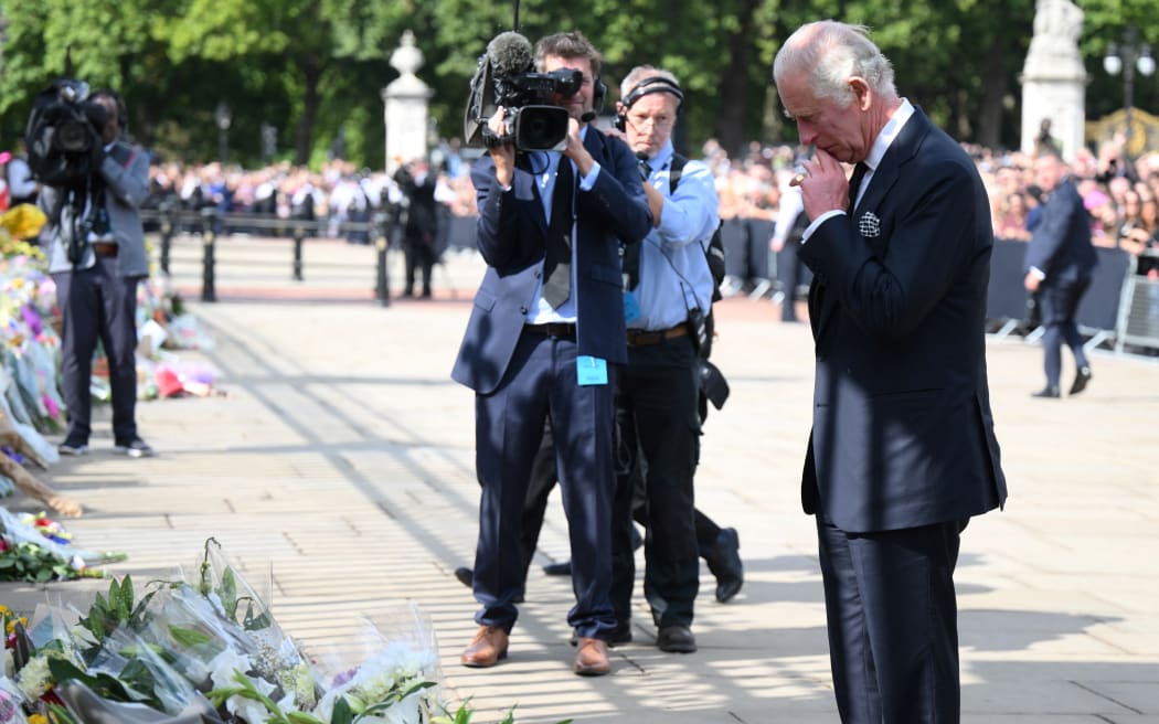 King Charles III looks at floral tributes left outside of Buckingham Palace in London, a day after Queen Elizabeth II died at the age of 96.