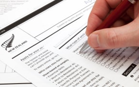 A man holding a ballpoint pen to fill a work visa application form to New Zealand.