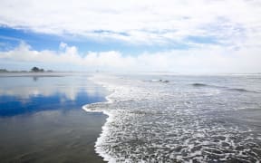 Coastline view on sky background in Westport of New Zealand. Soft waves splashing on sandy beach.