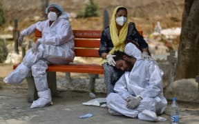An exhausted health worker wearing personal protective equipment rests at a bench at a graveyard, in Delhi, India