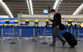 LONDON, ENGLAND - DECEMBER 21: Travellers wearing face coverings with their luggage in the almost deserted departures hall at Terminal 5 of Heathrow Airport in west London on December 21, 2020,