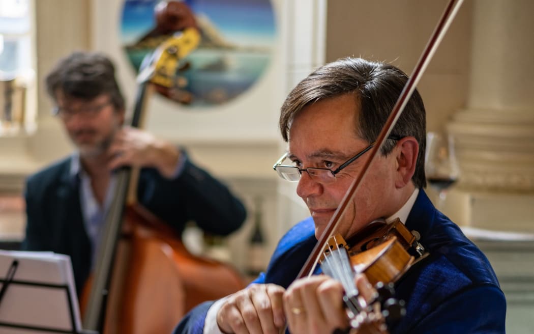 NZSO violinist Gregory Squire playing his instrument. A cellist accompanies him in the background.