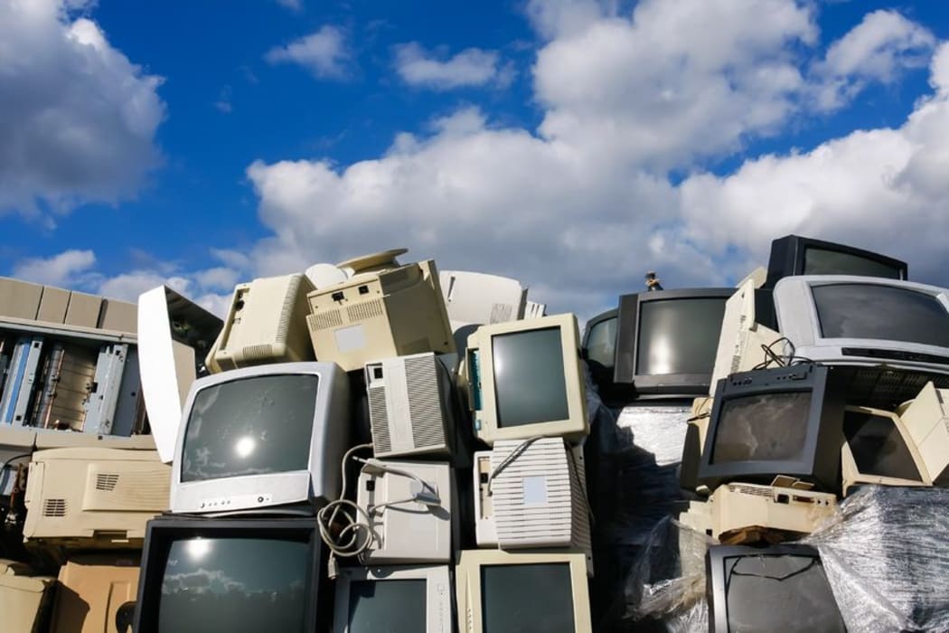 A pile of old computer screens  in a landfill, against a blue sky.